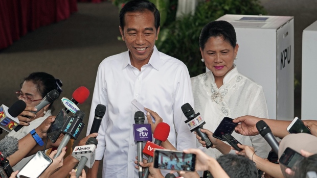 Joko Widodo, Indonesia's president, left, stands with his wife Iriana Joko Widodo while speaking to members of the media after casting their ballots at a polling station during the general election in Jakarta on April 17, 2019. 