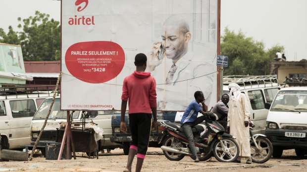 Pedestrians stand beside an advertisement for Bharti Airtel Ltd. in N'Djamena, Chad, on Tuesday, Aug. 15, 2017. African Development Bank and nations signed agreement to finance a project linking the town of Ngouandere in Cameroon and Chad’s capital, N’Djamena, according to statement handed to reporters in Cameroonian capital, Yaounde in July. 