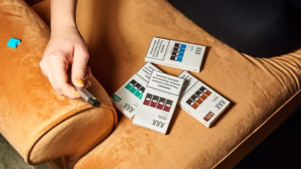 A person holds a Juul Labs Inc. e-cigarette next to packages of flavored pods in this arranged photograph taken in the Brooklyn Borough of New York, U.S., on Thursday, Dec. 20, 
