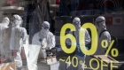 Workers wearing protective suits are reflected in a glass window of clothing store on Munjeong-dong Rodeo Street in the Songpa district of Seoul, South Korea, on Thursday, Feb. 27, 2020. More coronavirus cases were reported in other countries than in China for the first time, the World Health Organization said, a significant development highlighting the spread of the epidemic around the globe. The U.S. urged travelers to reconsider trips to South Korea as the country’s number of cases rose to more than 1,500. Photographer: SeongJoon Cho/Bloomberg