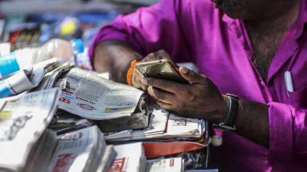 A vendor uses a smartphone while waiting for customers at a newspaper stand in Mumbai, India, on Saturday, Feb. 15, 2020. Facebook, YouTube, Twitter and TikTok will have to reveal users' identities if Indian government agencies ask them to, according to the country’s controversial new rules for social media companies and messaging apps expected to be published later this month. Photographer: Dhiraj Singh/Bloomberg