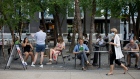 A woman walks by wearing a mask as people are seen at outdoor seating in Yorkville