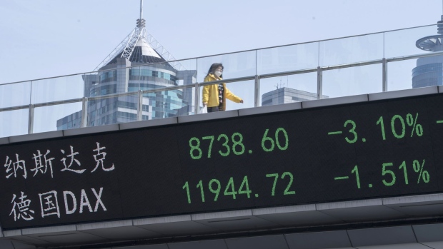 A pedestrian wearing a protective mask walks along an elevated walkway above an electronic ticker in Shanghai. Photographer: Qilai Shen/Bloomberg