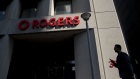 A pedestrian passes in front of Rogers Communications Inc. signage displayed outside a building in Toronto, Ontario, Canada, on Wednesday, May 17, 2017. Rogers Communications, Canada's largest wireless carrier, is leveraging organic growth in the country's wireless market to expand its subscriber base.