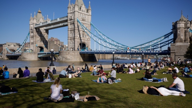 Pedestrians relax in the sunshine in a park on the south bank of the River Thames in view of Tower Bridge in London, U.K., on Monday, March 29, 2021. Starting Monday, six people, or two households, can gather outdoors and outdoor sports facilities such as tennis and basketball courts will be allowed to reopen. Photographer: Jason Alden/Bloomberg