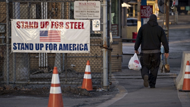 A man walks past a "Stand Up For Steel, Stand Up For America" sign while arriving at the United States Steel Corp. Clairton Plant coke manufacturing facility as emissions rise in Clairton, Pennsylvania.