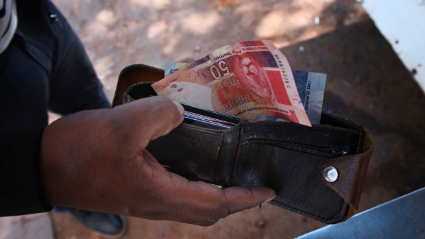 A customer with South African rand banknotes at a street vendor's stall in the Sandton district of Johannesburg, South Africa, on Friday, May 12, 2023. The rand slumped to its weakest level on record against the dollar and government bond yields soared as a diplomatic row between South Africa and the US simmered, putting trade of as much as 400 billion rand ($21 billion) at risk. Photographer: Leon Sadiki/Bloomberg