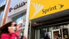 In this April 27, 2010 file photo, a woman using a cell phone walks past T-Mobile and Sprint stores 