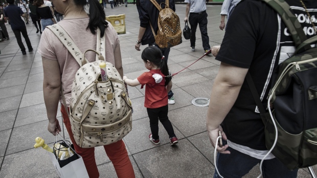 Pedestrians and a child wearing a child harness walks along a pedestrian shopping area in Shanghai, China, on Friday, Sept. 29, 2017. China's earliest economic indicators hinted that growth continued to moderate in September as official drives to curb debt risk and clear the skies weighed on activity. Photographer: Qilai Shen/Bloomberg