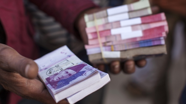 A roadside money changer handles bundles of Pakistani rupee banknotes at a currency exchange market in Karachi, Pakistan. 