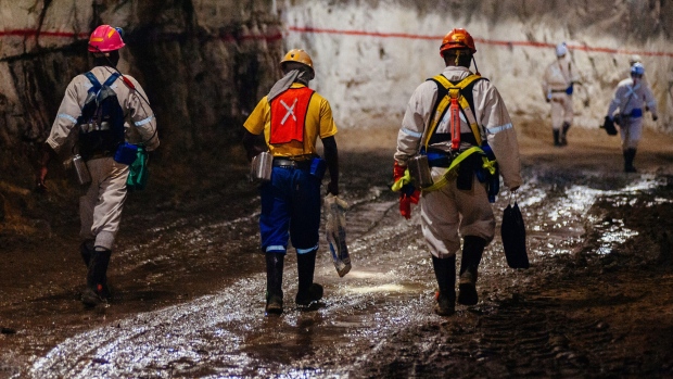 Miners wearing safety equipment walk through an underground tunnel 