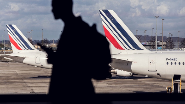 A passenger walks through the terminal as Tricolour livery sits on the tail fins of Air France passenger aircraft beyond, operated by Air France-KLM Group, as it stands on the tarmac at Charles de Gaulle airport, operated by Aeroports de Paris, in Paris, France, on Monday, Feb. 12, 2018. Air France will report its full year earnings on Feb 16. 