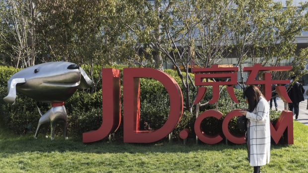 A woman stands next to signage incorporating the logo of JD.com Inc. and the company's mascot "Joy" at the company's headquarters in Beijing, China, on Monday, Oct. 23, 2017. JD.com is China's second-largest online mall. 