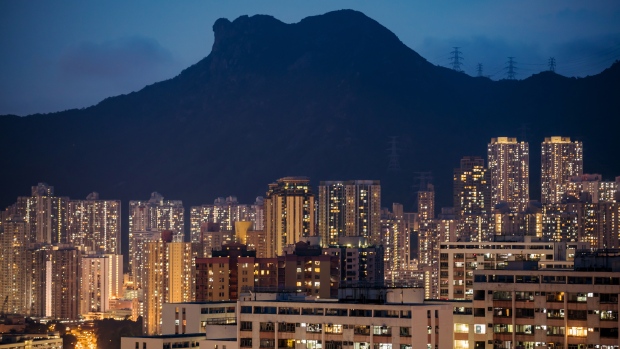 Residential buildings stand illuminated under Lion Rock at dusk in Hong Kong, China