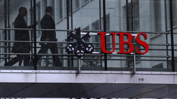 Employees pass between offices as UBS Group AG logo sits on a walkway at the UBS headquarters in Zurich, Switzerland. 