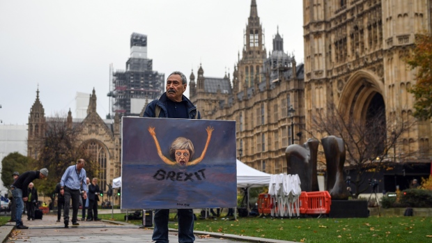 Kaya Mar, a political artist, holds a painting depicting Theresa May, U.K. prime minister, on College Green in London, U.K., on Thursday, Nov. 15, 2018. U.K. As Brexit Secretary Dominic Raab resigned, Prime Minister Theresa May is fighting for her political life as a growing revolt from within her own party threatens to derail her Brexit plans and force the U.K. out of the European Union with no deal. 