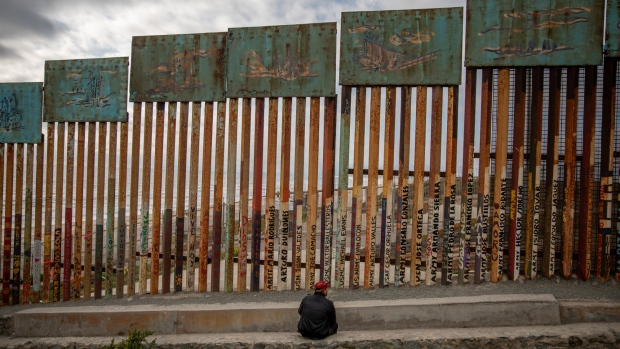 A person sits in front of a section of the U.S.-Mexico border wall in Tijuana, Mexico, on Saturday, May 19, 2018. 