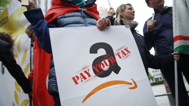 BERLIN, GERMANY - APRIL 24: An activist holding a sign demanding online retailer Amazon pay its share of taxes joins a protest gathering outside the Axel Springer building on April 24, 2018 in Berlin, Germany. Several hundred Amazon warehouse workers from Germany, Poland and Italy protested outside the Axel Springer building, where inside Bezos was scheduled to receive an award for innovation. The workers claim Amazon pays too little and offers too few benefits. (Photo by Sean Gallup/Getty Images)