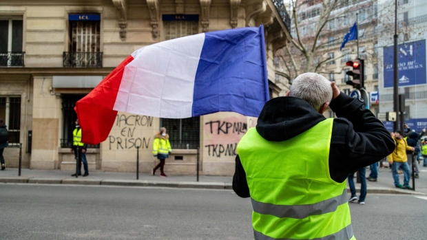 A demonstrator wearing a yellow vest (Gilets jaunes) waves a French national flag in front of the Arc de Triomph during protests in Paris, France on Saturday, Dec. 8, 2018. French police arrested 317 people across Paris early Saturday, ahead of planned protests by the “Yellow Vests” movement in the French capital, seeking to prevent violent clashes between rioters and police forces seen a week ago on and around the Champs-Elysees. Photographer: Anita Pouchard Serra/Bloomberg