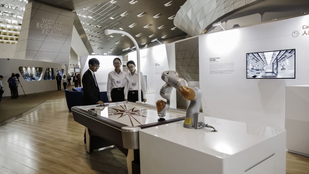 Attendees stand opposite a Kuka LBR iiwa robotic arm at an air hockey table at the World Economic Forum (WEF) Annual Meeting of the New Champions in Dalian, China, on Wednesday, June 28, 2017. The forum runs through to June 29. Photographer: Qilai Shen/Bloomberg