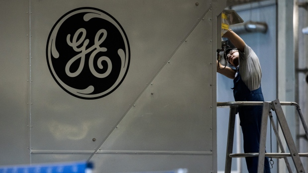 A GE logo sits on a panel as an employee works inside the General Electric Co. power plant in Veresegyhaz, Hungary, on Tuesday, June 13, 2017. General Electric won approval on Monday from the U.S. Justice Department to combine its oil and gas business with Baker Hughes Inc. 