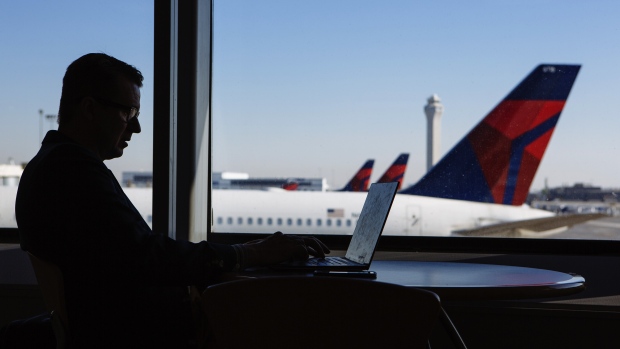 A traveler works on a laptop computer as Delta Air Lines Inc. planes are seen outside a window at Salt Lake City International airport (SLC) in Salt Lake City, Utah, U.S., on Friday, July 6, 2018. Delta Air Lines Inc. is scheduled to release earnings figures on July 12. 