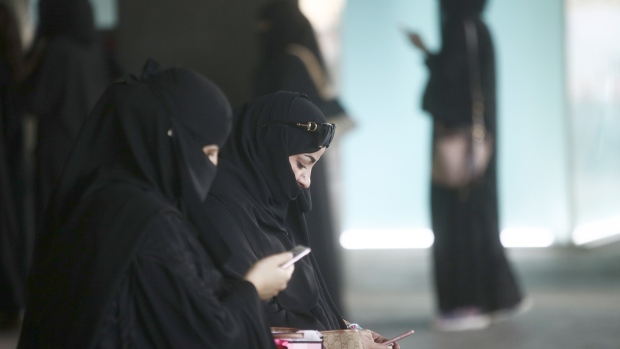 Female shoppers wearing traditional Saudi Arabian dress check their smartphones whilst waiting for transport outside a store at the Kingdom Centre shopping mall in Riyadh, Saudi Arabia. 