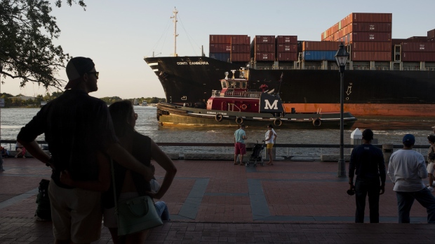 Pedestrians watch from River Street as a cargo ship and a tug boat travel into the Port of Savannah on the Savannah River in Savannah, Georgia, U.S. 