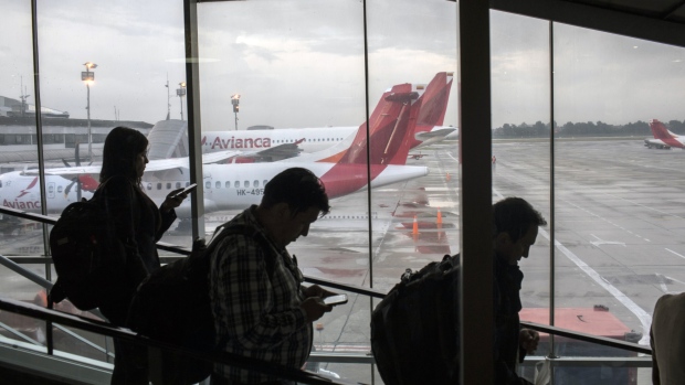 Travelers move down an escalator in front of Avianca Holdings SA passenger airplanes sitting on the tarmac at El Dorado International Airport (BOG) in Bogota, Colombia, on Tuesday, Oct. 31, 2017. Avianca Holdings SA reported a net income of $36.1 million USD in the third quarter despite a pilot strike that lasted for almost two months. 