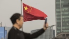 A Chinese national flag flies as a man uses a smartphone in Shanghai, China, on Tuesday, Nov. 27, 2018. Apple, which has lost a fifth of its value in a tech market rout since October, is poised for another setback after U.S. President Donald Trump suggested that 10 percent tariffs could be placed on mobile phones, like the iPhone, and laptops made in China. 