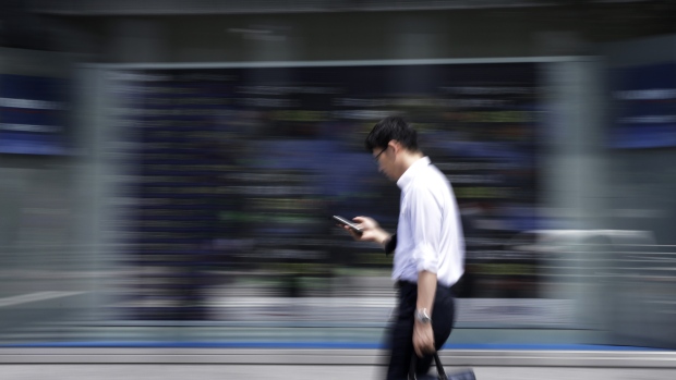 A pedestrian using his smartphone walks past an electronic stock board outside a securities firm in Tokyo, Japan. 