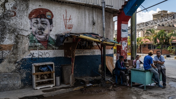 People sit next to a mural of the late Hugo Chavez in the Petare neighborhood of Caracas. 