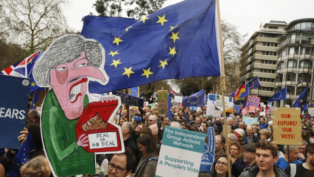 Demonstrators carry a placard depicting Theresa May, U.K prime minister, and European Union flags as they march during the anti-Brexit People's Vote rally in London, U.K., on Saturday, March 23, 2019. The campaign to give U.K. citizens a vote on U.K. Prime Minister Theresa May's Brexit deal, twice defeated by Parliament, holds the rally after European Union leaders gave May an extra two weeks to work out what to do. 