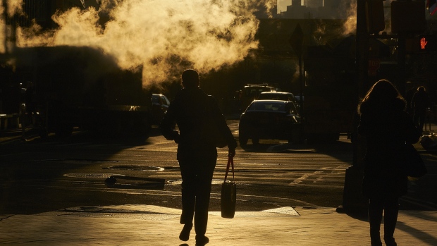 Steam rises past pedestrians walking along a street near the New York Stock Exchange. 