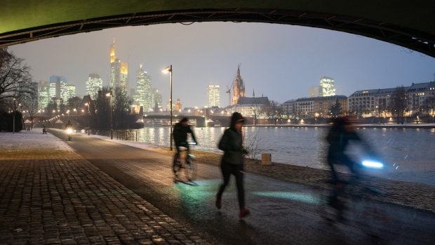 A jogger and cyclists pass along a towpath as skyscrapers stand illuminated on the skyline beyond the River Main in Frankfurt, Germany, on Thursday, Jan. 24, 2019. ECB President Mario Draghi intensified his warning on the challenges facing the euro-area economy, signaling the European Central Bank could be even more cautious about any withdrawal of crisis-era stimulus this year. 