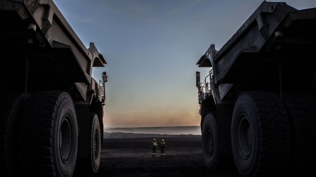 Workers stand near dump trucks at a mine. 