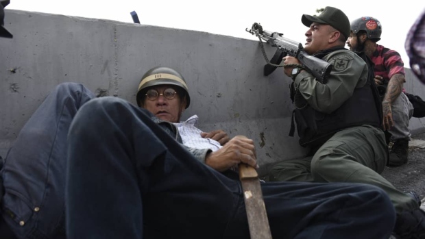 A protester takes cover behind a concrete barrier beside a National Guard member supporting Venezuelan opposition leader Juan Guaido during a military uprising near the La Carlota base in Caracas on April 30, 2019. Photographer: Carlos Becerra/Bloomberg