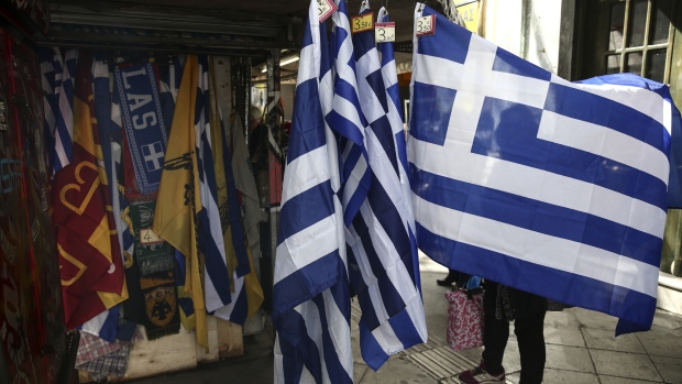 A woman unfolds a souvenir Greek national flag hanging outside a street vendor's kiosk in Athens, Greece, on Tuesday, Feb. 28, 2017. Greeces auditors are pulling together a list of policies the country needs to implement to unlock additional bailout funds as talks with Athens resumed on Tuesday, two people familiar with the matter said. 