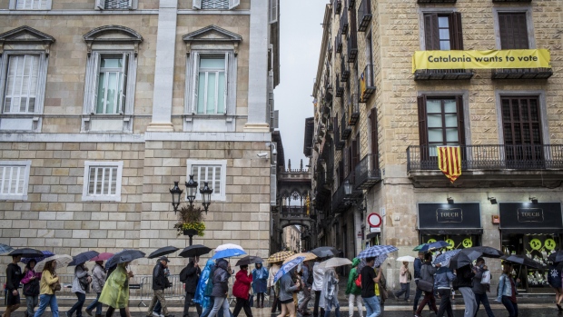 Tourists walk in the rain across Sant Jaume square, past the Generalitat regional government offices in Barcelona, Spain, on Thursday, Oct. 19, 2017. Spain’s government issued a statement on Thursday morning invoking Article 155 of the Constitution “to restore the legality” of the semi-autonomous region. 