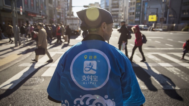 A staff member wearing a uniform featuring the logo for Ant Financial Services Group's Alipay, an affiliate of Alibaba Group Holding Ltd., stands during a campaign event in Tokyo, Japan, on Saturday, Dec. 9, 2017. Ant Financial and its strategic partners outside China should be able to nearly double users of their payments systems in coming years, Ant's overseas operations president Douglas Feagin said on Nov. 14. 