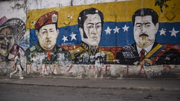 A pedestrian passes in front of a mural depicting the late Hugo Chavez, Simon Bolivar, and Nicolas Maduro, Venezuela's president, in the Palo Verde neighborhood of Caracas. 
