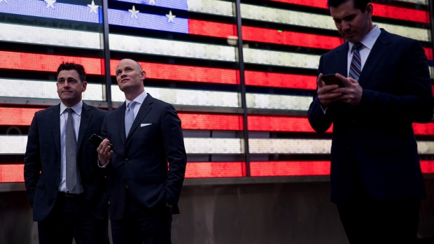 Pedestrians stand in front of an illuminated American flag in the Times Square neighborhood of New York. 