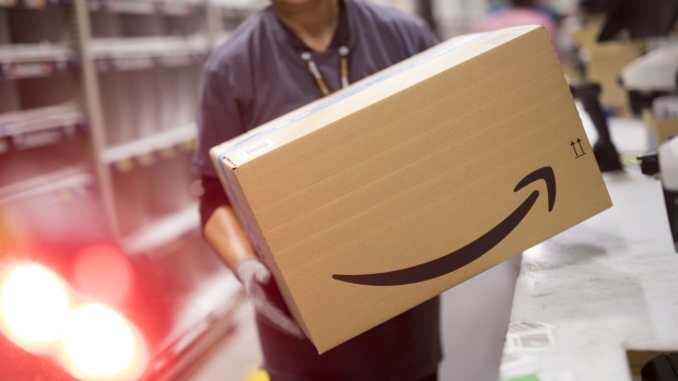 An employee carries a box at the Amazon.com Inc. fulfilment centre in Tilbury, U.K. on Friday, July 12, 2019. By offering 12 extra hours of deals during this year's Prime Day, Amazon will pull in nearly 50% more in sales, according to an estimate from Coresight Research. 