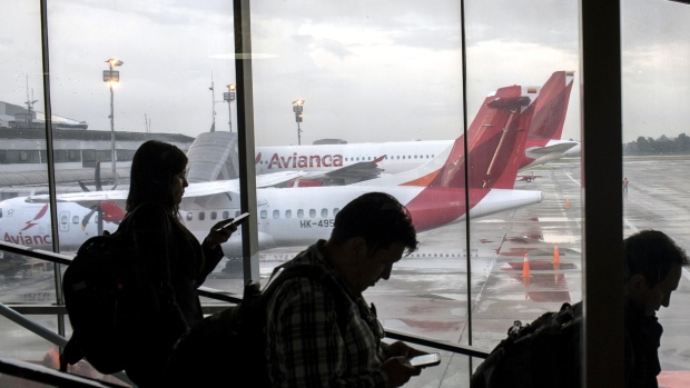 Travelers move down an escalator in front of Avianca passenger airplanes sitting on the tarmac at El Dorado International Airport in Bogota. 