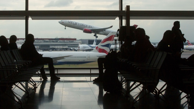 Passengers sit in a terminal as a passenger aircraft, operated by Virgin Atlantic Airways Ltd., takes off at London Heathrow airport in London, U.K., on Friday, Oct. 7, 2016. Europe's busiest hub is stepping up its pitch for a new runway with a much-delayed U.K. government decision on where to locate additional flight capacity for southern England likely to announced in the coming weeks. 
