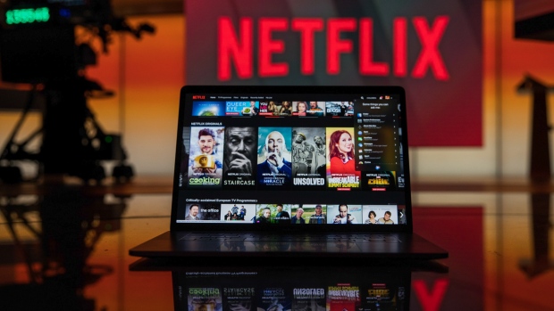 A laptop computer screen displaying the Netflix homepage stands against an illuminated screen bearing the company logo in this arranged photograph in London, U.K., on Tuesday, June 26, 2018. 