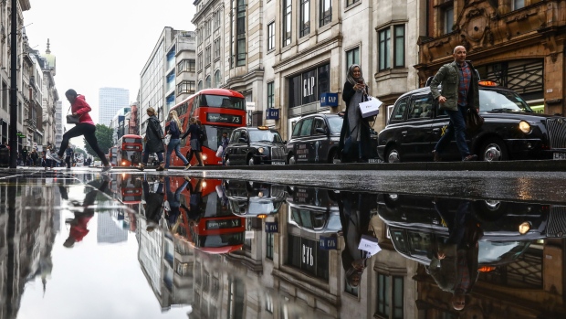 A puddle reflects pedestrians, buses, taxis and a The Gap Inc. retail store on Oxford Street in London, U.K., on Tuesday, May. 29, 2018. U.K. consumer confidence slid this month as Britons felt less secure about their jobs and the value of their houses. 