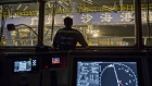 A crew member surveys the loading of shipping containers from the control room of a container ship b