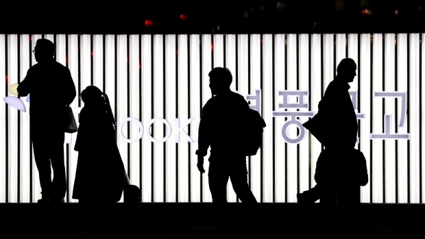 People are silhouetted as they walk past an illuminated neon sign near the Cheonggyecheon stream at night in Seoul. 