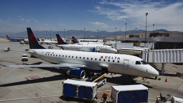 A ground crew member moves luggage carts in front of a Delta Air Lines Inc. Connection plane at Salt Lake City International airport (SLC) in Salt Lake City, Utah, U.S., on Thursday, July 5, 2018. Delta Air Lines Inc. is scheduled to release earnings figures on July 12. 